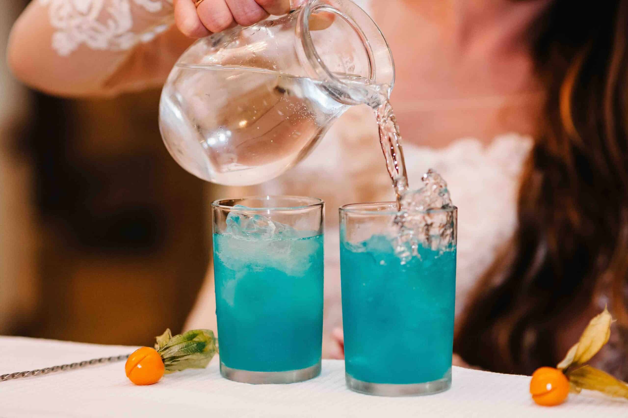 The bride pours a cocktail. Woman hand pours fresh blue juice in the glass making the cocktail on the bar counter at night club.